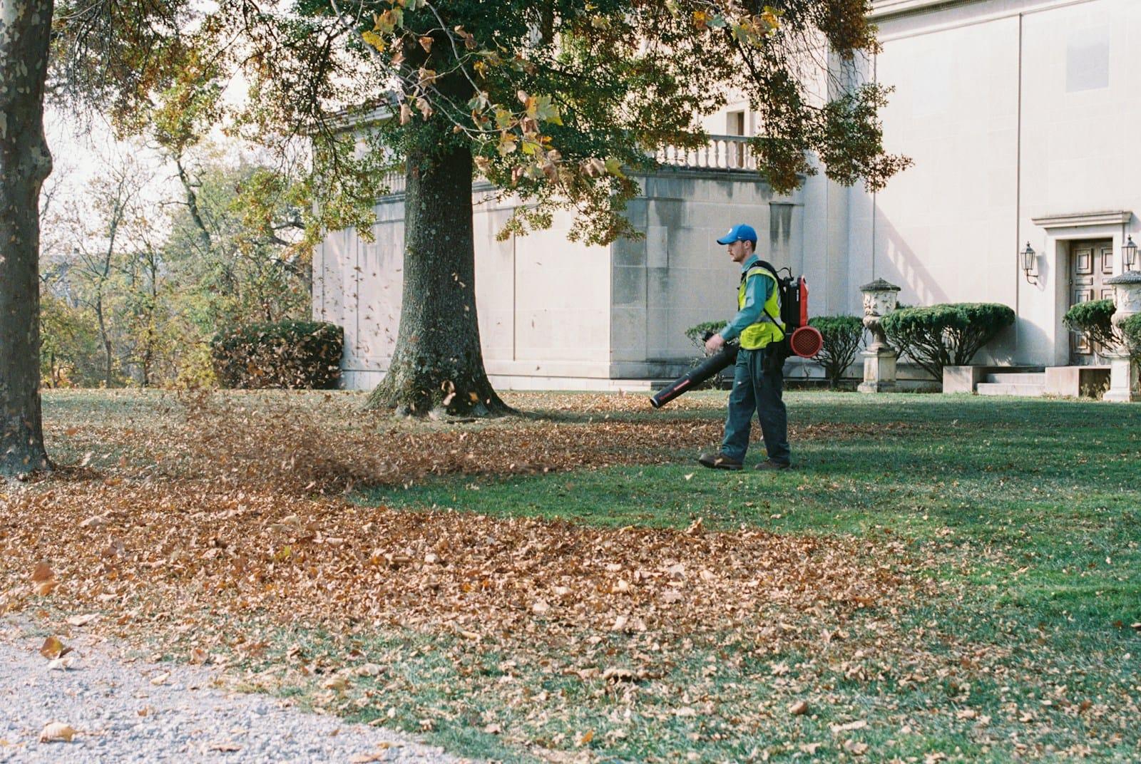 Worker clearing fall leaves from a lawn with a backpack blower
