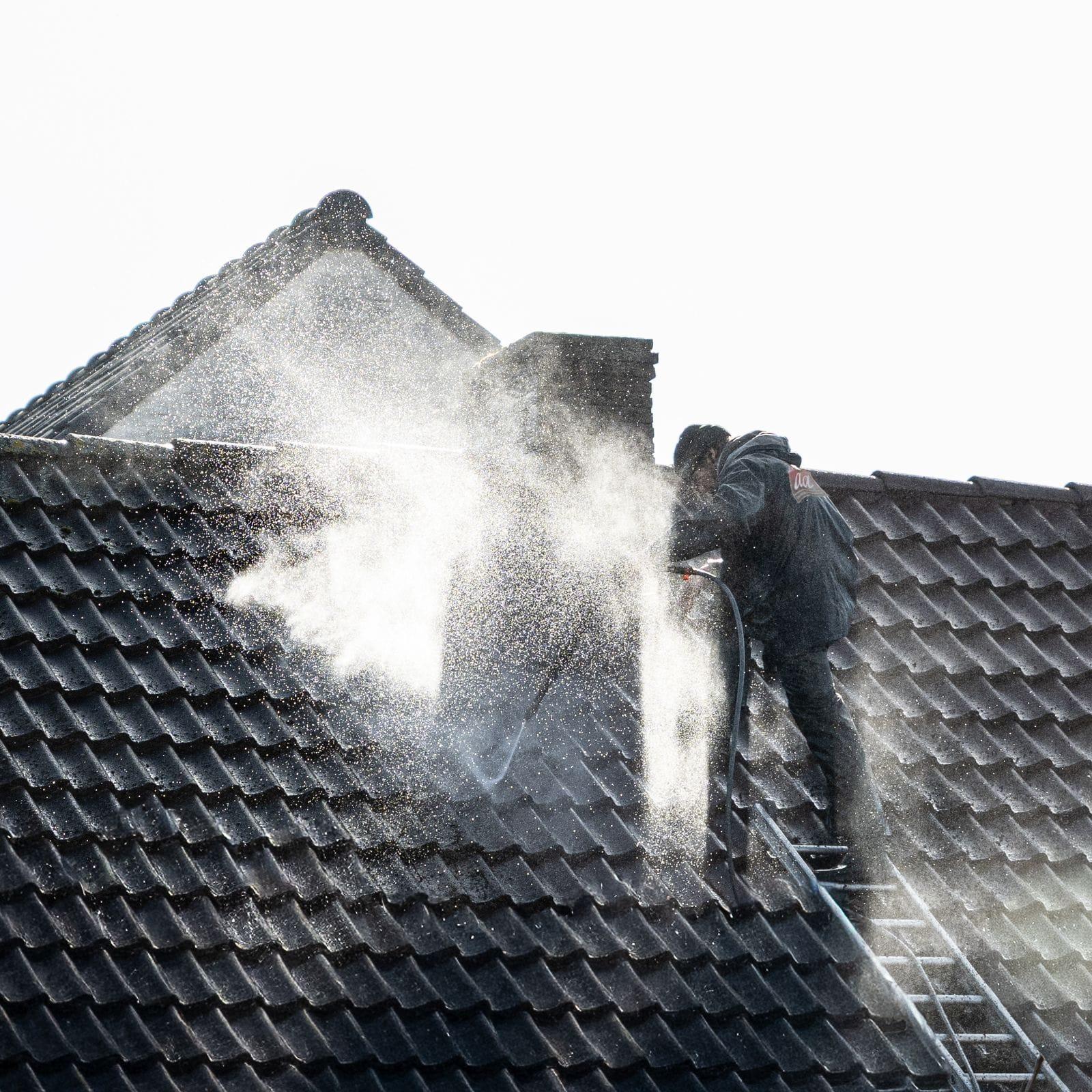 Worker pressure washing algae and grime off a home exterior